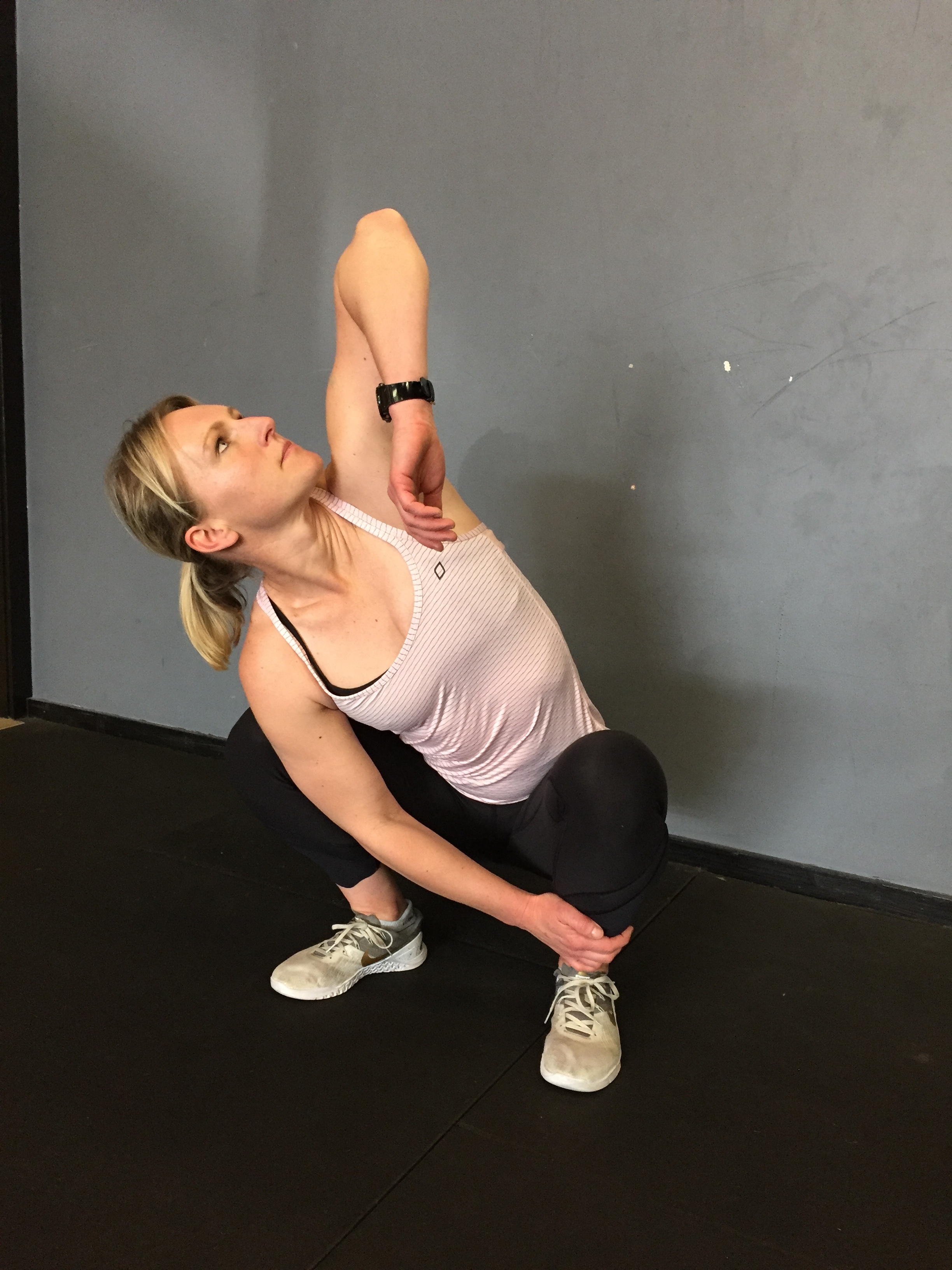 In a deep squat, hold your opposite ankle with one hand, and point the other elbow up toward the ceiling